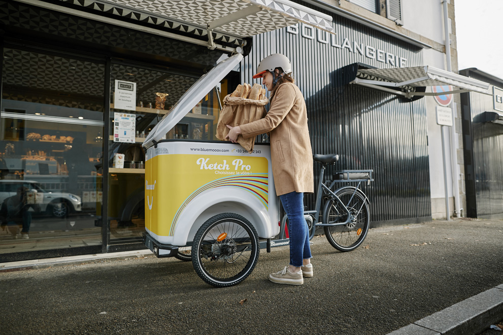 Vélo cargo triporteur Bluemooov Ketch à assistance électrique devant une boulangerie